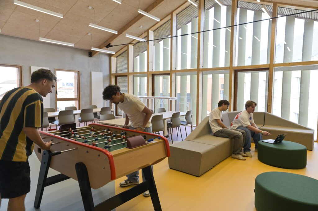 Le hall sous sa charpente : baby‑foot, banquettes et étudiants au travail