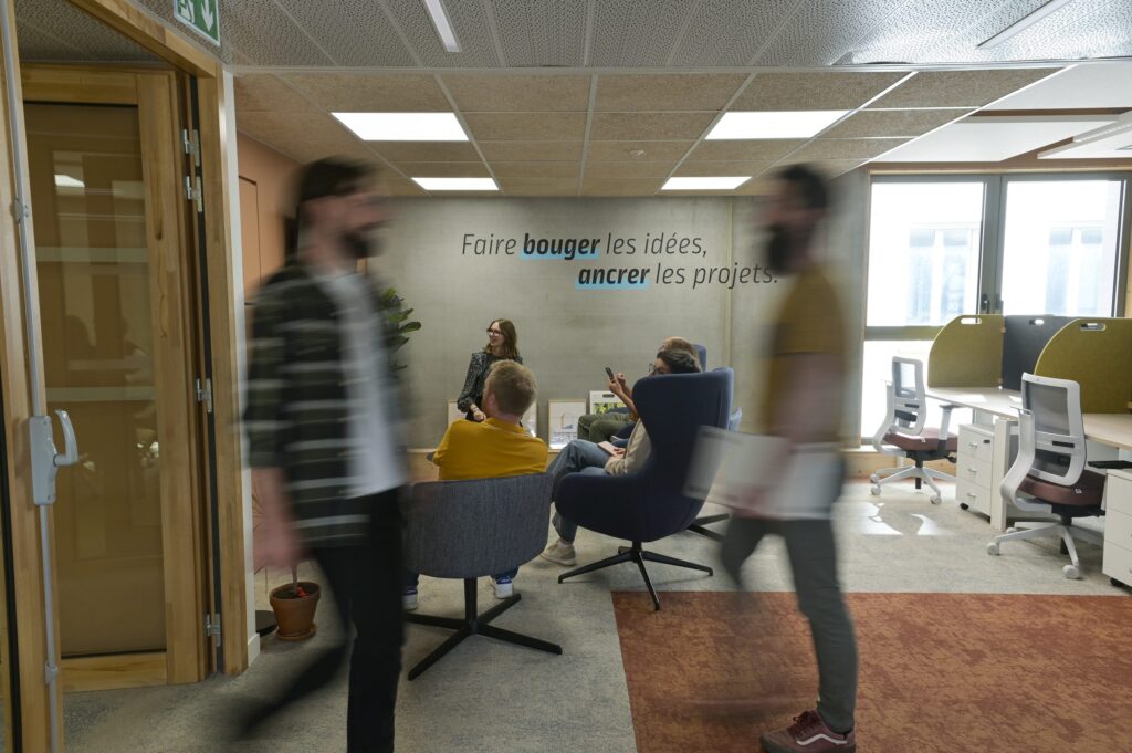 Un espace de travail de la pépinière, fauteuils bas et postes ouverts, devant le mur « Faire bouger les idées, ancrer les projets »